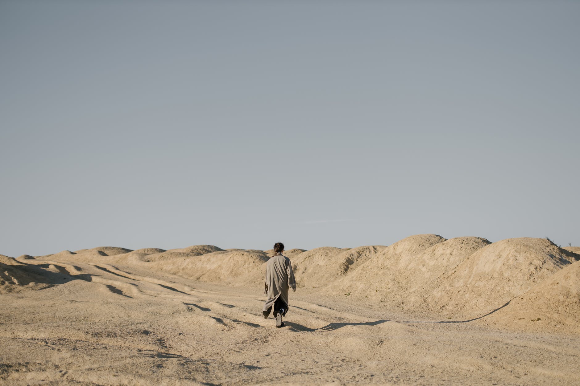 man in gray jacket walking on brown sand